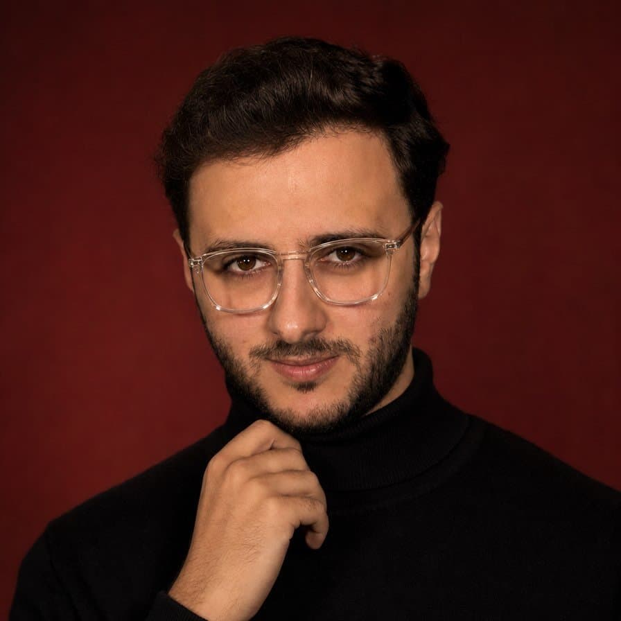 Portrait of Saif Ziyad in a black turtleneck against a deep red backdrop